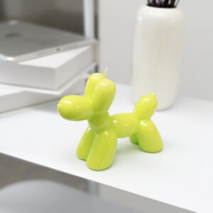 The Balloon Dog Candle - Lime adds playful charm to modern, minimal spaces as it sits on a white tabletop near books and a vase—an eye-catching decor piece, ideal for gift shops. Gate21.ee