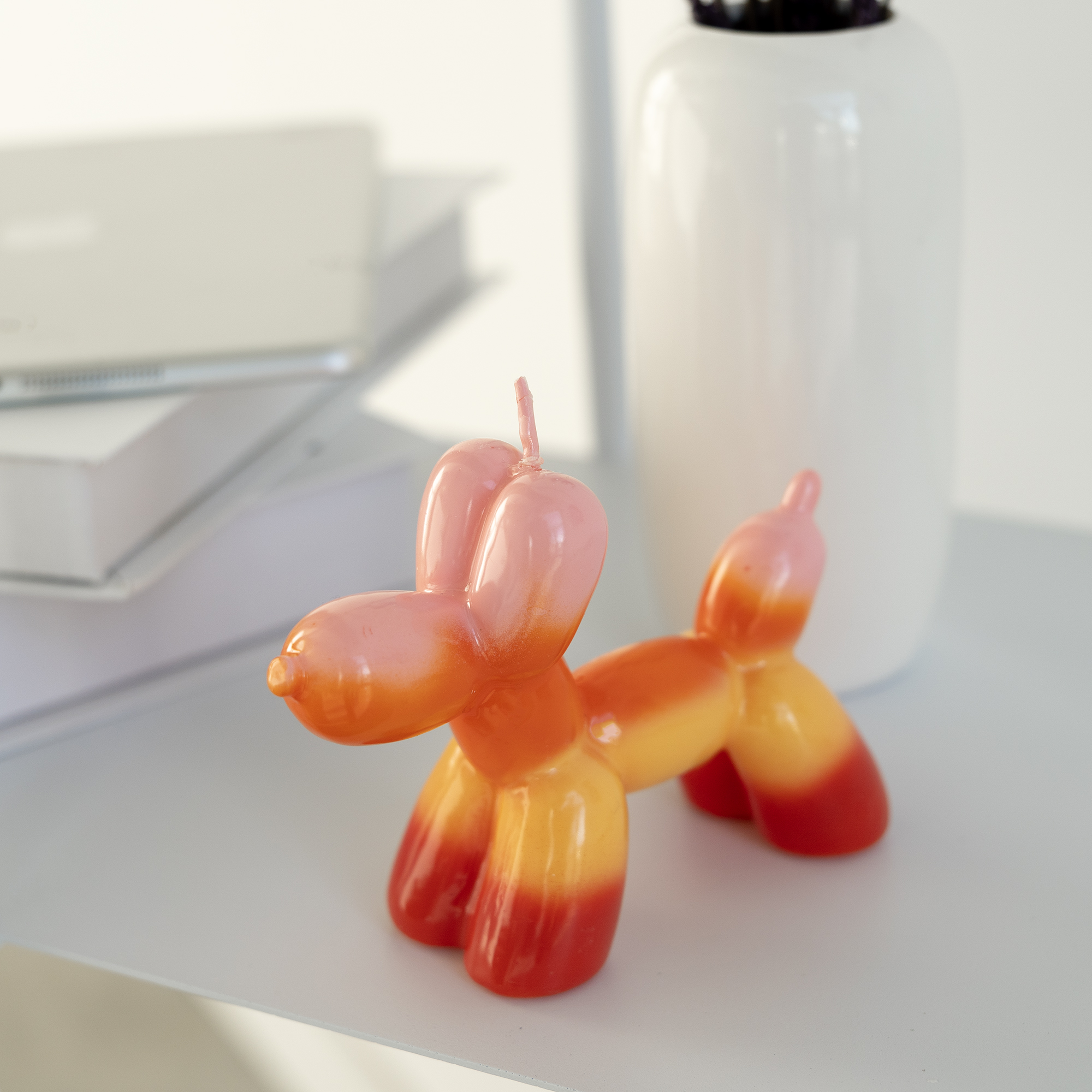 The Balloon Dog Candle - Lime sits on a white surface next to stacked books and a white vase—perfect for anyone seeking unique gifts or fans of Estonian design from Tallinn shopping adventures. Gate21.ee