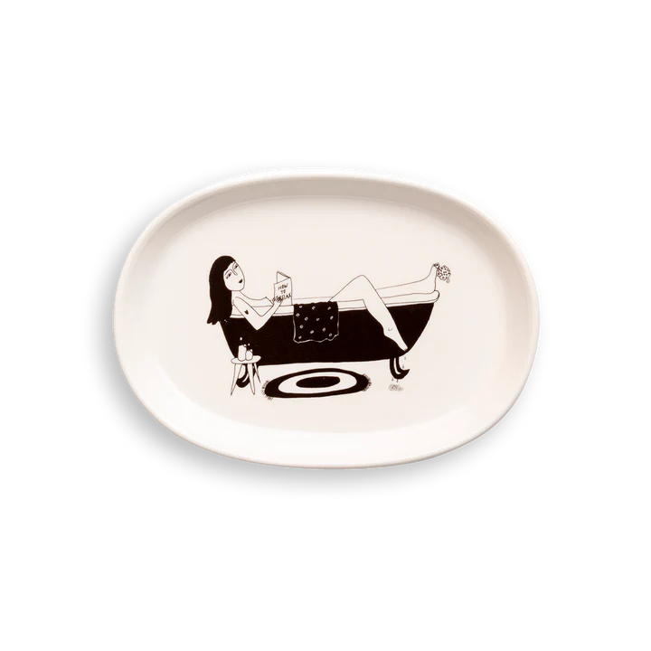 The "How to Relax - Tray" is a white oval plate with a black line drawing of a woman in a bath, drink and book in hand—an Estonian design gem perfect for anyone looking for unique Tallinn shopping finds. Gate21.ee