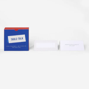 A blue and red Table Talk Cards box is placed next to two white cards—one with subtle stripes, one with printed text—on a white background, capturing the modern simplicity typical of Estonian design seen in Tallinn’s concept shops. Gate21.ee