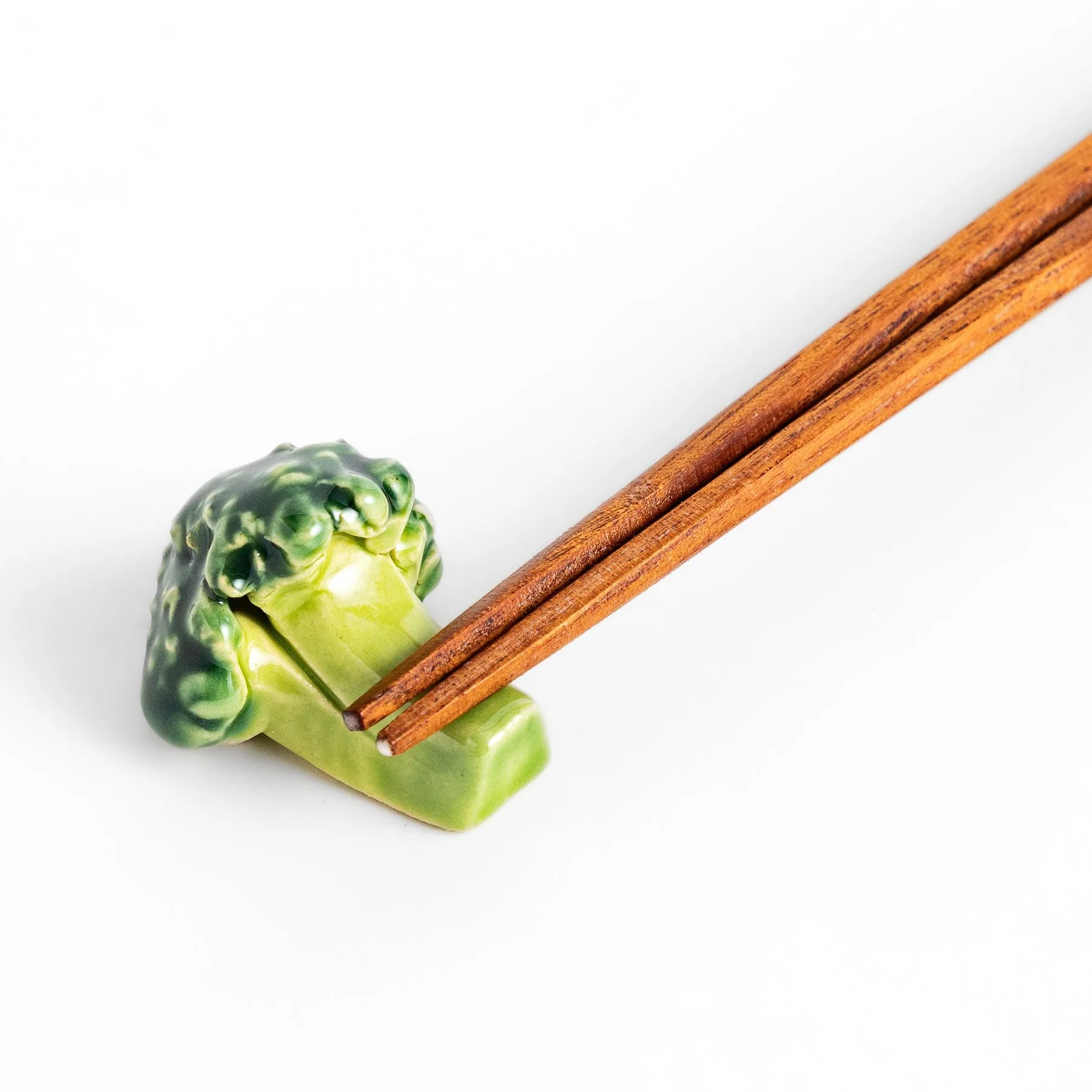 A pair of wooden chopsticks rests on a Japanese Chopstick Rest - KÕIK, designed to resemble broccoli, highlighting curated Estonian design against a plain white background. Gate21.ee
