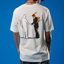 A person wears the Burn Tee - Bone, a white T-shirt with an Estonian graphic on the back: a cartoon suited figure on fire shaking hands with a cat-like character against solid blue—ideal for curated Tallinn shopping finds. Gate21.ee