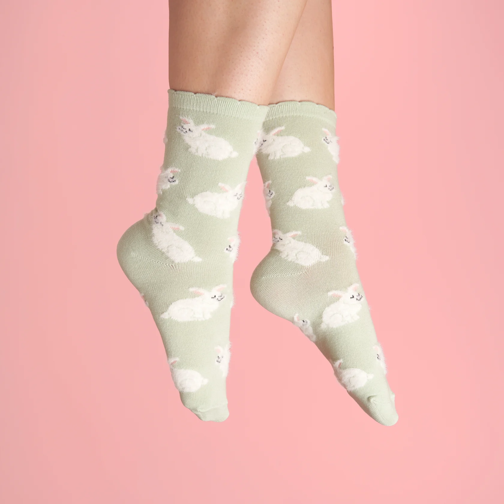 A pair of feet in Rabbits - Grey Cotton Socks, featuring a cute bunny pattern, shown against a pink background—ideal for fans of Estonian design and unique concept shop finds. Gate21.ee