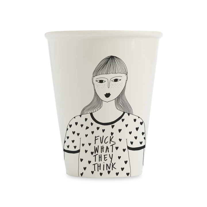 The F*ck What They Think cup features a black and white illustration of a woman with straight hair and fringe, wearing a heart-patterned shirt with the bold text "FUCK WHAT THEY THINK." A unique piece of Estonian design. Gate21.ee