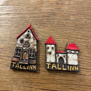 Two small Raivo Koit keraamika - K&Otilde;IK ceramic magnets shaped like buildings with red roofs and "Tallinn" at the bottom, ideal for collectors or as unique Tallinn souvenirs, displayed on a wooden surface. Gate21.ee
