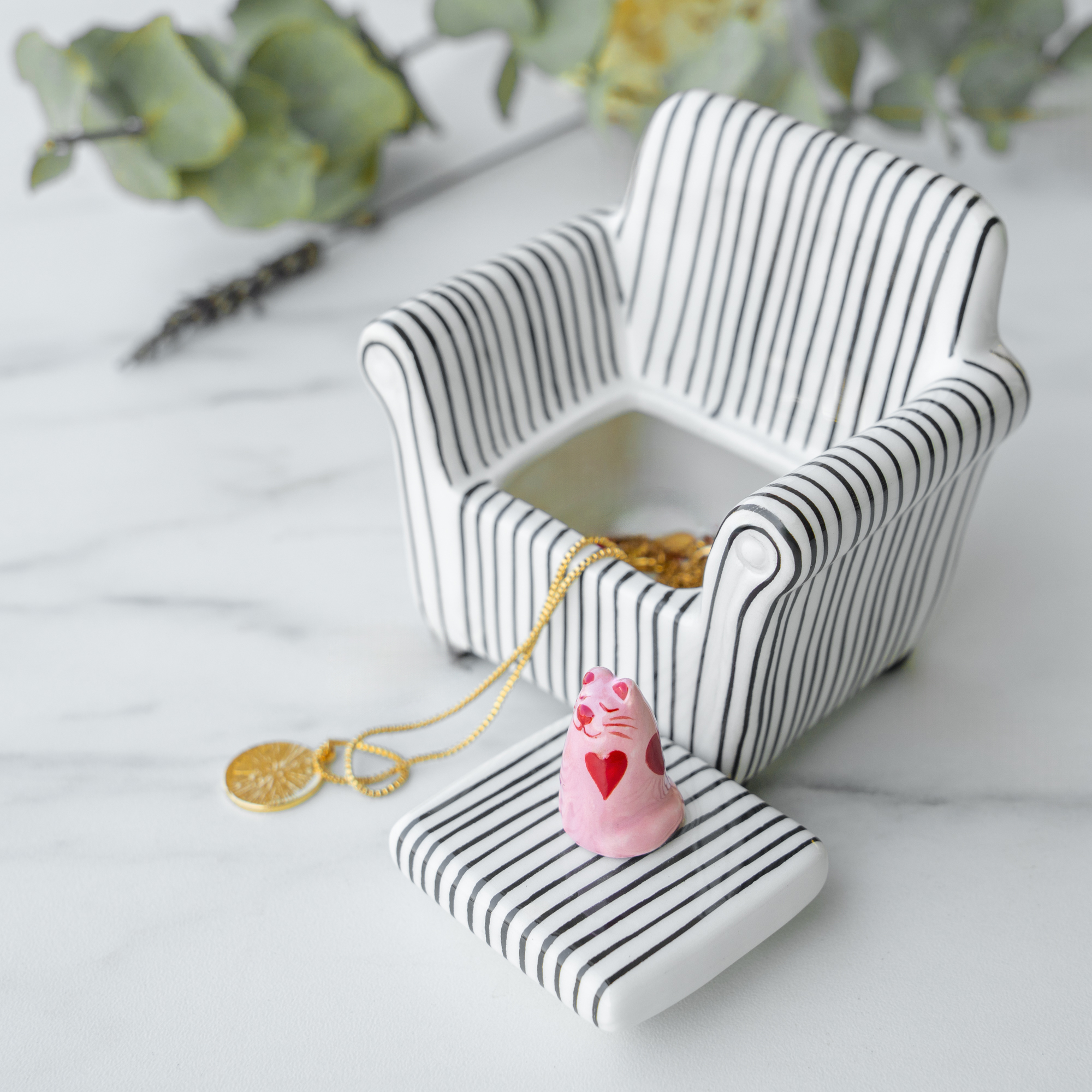 The Blue Chair - Jewellery Box is a unique ceramic chair in blue with a removable seat cushion, containing two gold coins, a gold necklace, and a small pink heart figurine—perfect for curated Tallinn gift shops. Gate21.ee