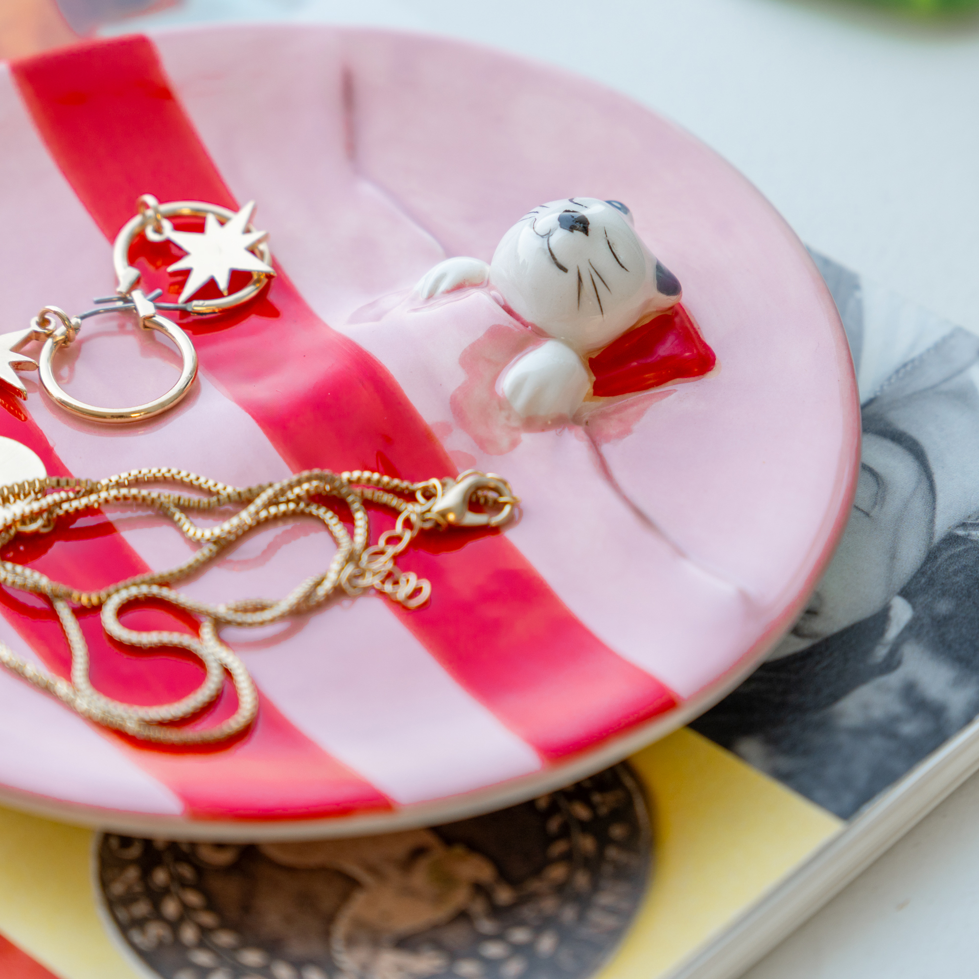 The Pink Dreamer Cat - Jewellery Plate, a curated Estonian ceramic dish with pink and red stripes, features a gold-accented cat figurine lying under a blanket—ideal for holding jewellery and perfect for Tallinn shopping enthusiasts. Gate21.ee