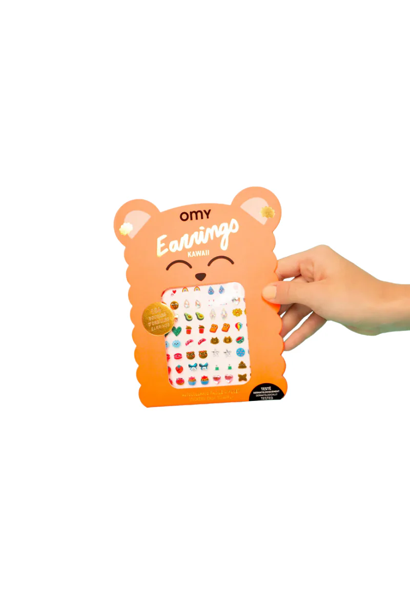 A hand holds an orange, bear-shaped package labelled Kawaii - Earring Stickers, showing multiple pairs of colourful, stick-on earrings with cute designs—ideal for gift shop lovers looking for unique ideas. Gate21.ee