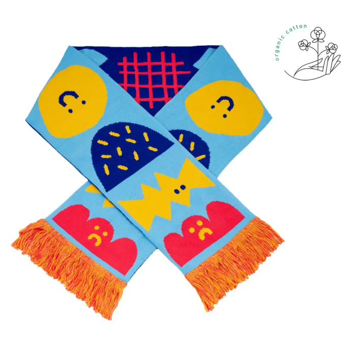 Moodies - Organic is a vibrant scarf with blue, yellow, and red abstract shapes and faces, orange fringe, and a white background. Made from organic cotton, it’s a unique accessory perfect for Tallinn shopping or as a special gift shop find. Gate21.ee