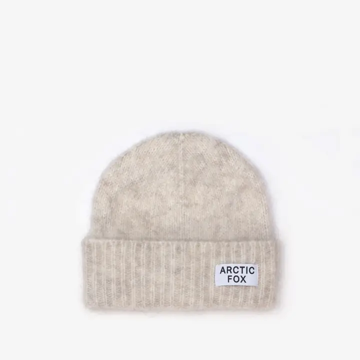 The Mohair Beanie - Alpine Ecru is a light beige knitted hat with a folded brim and a white rectangular ARCTIC FOX patch in black text on the front. Ideal for fans of classic Arctic Fox beanies, shown against a plain white background. Gate21.ee