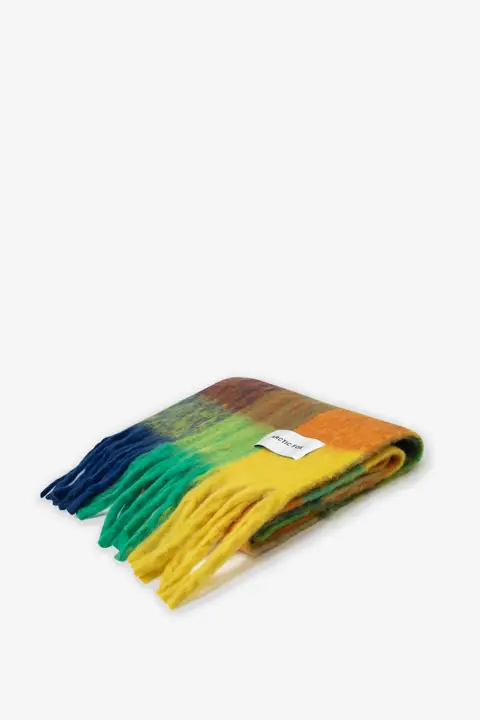 The Reykjavik Scarf - Nordic Skies, a multicoloured fringed accessory in shades of blue, green, yellow, and orange with a small white label, is neatly folded on a white background. Gate21.ee