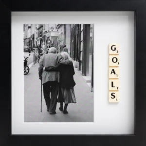The GOALS - Scrabble Print features a black-and-white photo of an elderly couple walking arm in arm, with Scrabble tiles spelling “GOALS” vertically inside a black frame—a meaningful piece to evoke memories and inspiration. Gate21.ee