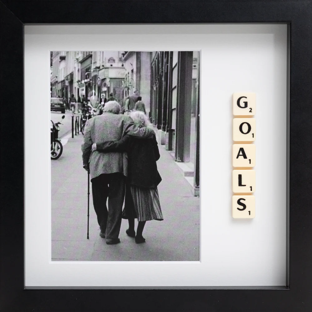 The GOALS - Scrabble Print features a black-and-white photo of an elderly couple walking arm in arm, with Scrabble tiles spelling “GOALS” vertically inside a black frame—a meaningful piece to evoke memories and inspiration. Gate21.ee
