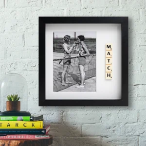 The "MATCH - Scrabble Print" features a framed black and white photo of two women with tennis racquets drinking by the net, with Scrabble tiles spelling MATCH—ideal wall décor above books and a plant in a glass dome. Gate21.ee