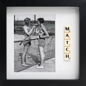 The MATCH - Scrabble Print features a black-and-white photo of two women in swimsuits on a tennis court, exchanging a racquet, with "MATCH" spelt out in Scrabble tiles—a unique piece to recall your favourite moments. Gate21.ee