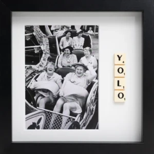 The YOLO - Scrabble Print features a framed black-and-white photo of women laughing on a rollercoaster, with Scrabble tiles spelling "YOLO"—a perfect piece to spark memories and celebrate moments that matter. Gate21.ee