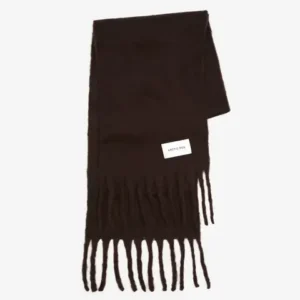 The Reykjavik Scarf - Ground Coffee is a dark brown scarf with long fringe at both ends and a rectangular white label sewn on one side, shown against a plain white background. Gate21.ee