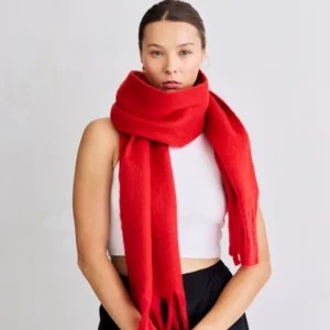 A person stands against a plain background wearing the Stockholm Scarf - Crimson Red wrapped around their neck, paired with a white sleeveless top and black trousers. Gate21.ee