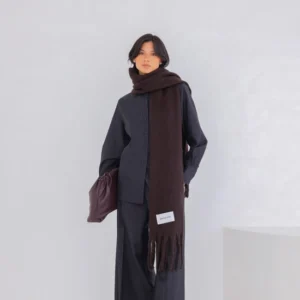 A person stands against a plain white background wearing a dark button-up shirt, wide-leg trousers, leopard print shoes, and the Reykjavik Scarf in Ground Coffee, holding a dark-coloured bag under one arm. Gate21.ee
