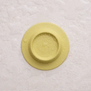 The Soapi - Yellow silicone object, featuring a round design and water droplets on its surface, is shown on a light textured background. Gate21.ee