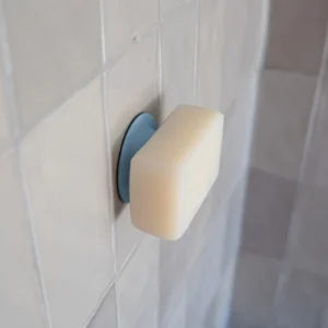 A rectangular Soapi - Light Blue bar is magnetically attached to a round metal holder on glossy, light-coloured tiled walls, adding a modern touch. Gate21.ee