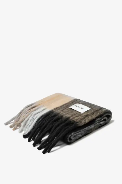 A folded The Stockholm Scarf - The Arctic with a beige, grey, and black gradient and fringe, plus a white rectangular label on one side, displayed against a plain white background. Gate21.ee