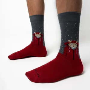 Someone wearing Raining Cat - Grey Jimmy Lion socks with a cat’s face, starburst pattern, and white dots. The red and grey socks cover the ankles and lower calves, set against a plain white background. Gate21.ee