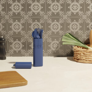 The Bini Cutlery Kit - Night stands upright on a kitchen worktop beside a wooden chopping board, wicker basket with vegetables, and pepper mill, set against a backdrop of patterned grey tiles. Gate21.ee