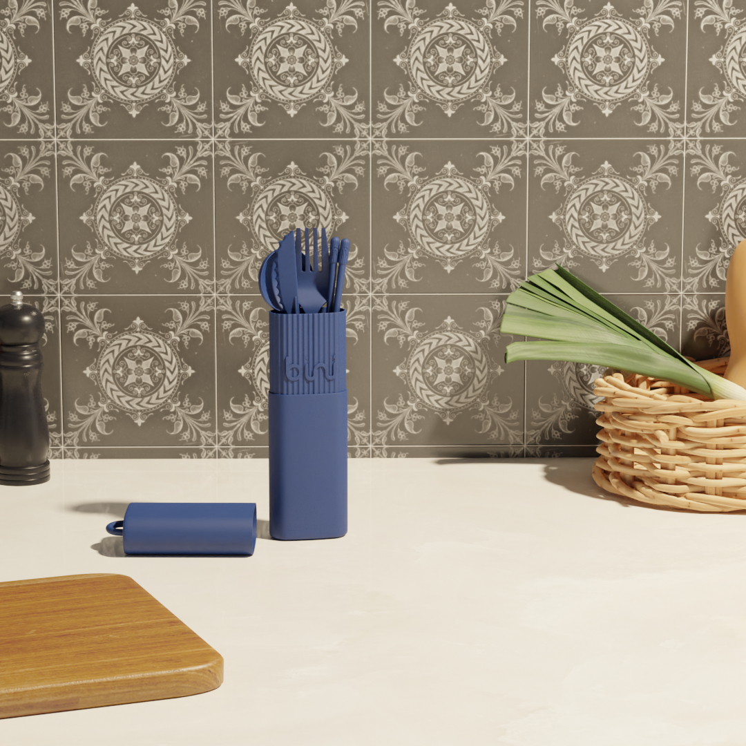 The Bini Cutlery Kit - Night stands upright on a kitchen worktop beside a wooden chopping board, wicker basket with vegetables, and pepper mill, set against a backdrop of patterned grey tiles. Gate21.ee