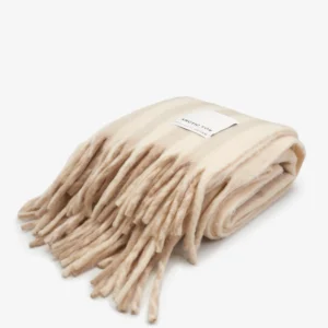 A folded pale taupe Wool Stripe Throw blanket with long fringe tassels, featuring a white rectangular label on top, displayed on a plain white background. Gate21.ee