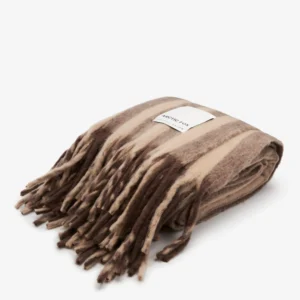 A folded The Wool Stripe Throw - Pale Taupe, made of wool with brown and beige stripes, long fringed edges, and a white rectangular label sewn on top. Gate21.ee