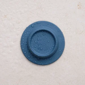 A round, dark blue Soapi – Petrol with water droplets on its surface is displayed against a textured, light beige background. Gate21.ee