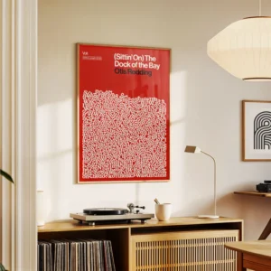 A bright, modern room with minimalist decor features a (Sittin&rsquo; on) The Dock of the Bay - Lyrics Poster with a red frame above a record player on a wooden sideboard. Gate21.ee