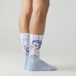 A person wears light blue Roy Lichtenstein Girl with Hair Ribbon - Athletic socks, featuring a woman's face and shoulders with a blue grid pattern, standing on a light grey surface. Gate21.ee