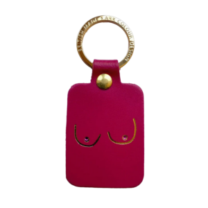 The Boob Key Ring - Magenta is a rectangular pink leather keyring with a gold metal ring and stud. It features a minimalist line drawing of breasts, accented with small crystals as nipples for a playful, chic look. Gate21.ee