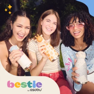 Three young women sit outside, smiling and holding 740ml Kitty Bestie bottles. The bottom corner shows "bestie by asobu" in colourful letters, with playful graphic accents decorating the image's corners. Gate21.ee
