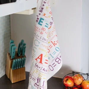 The Equations - Tea Towel from the Unemployed Philosophers Guild, featuring colourful maths equations and symbols, hangs from a cupboard handle by the microwave above a knife block, wire fruit basket with apples, and hob. Gate21.ee