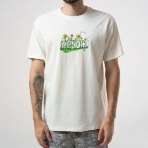 A person wears the Flower Boy Tee - Bone, featuring RipnDip’s playful style with yellow flowers, green grass, the word FRIENDS, and a white cat on the chest. The cream-coloured tee leaves their arms partially visible. Gate21.ee