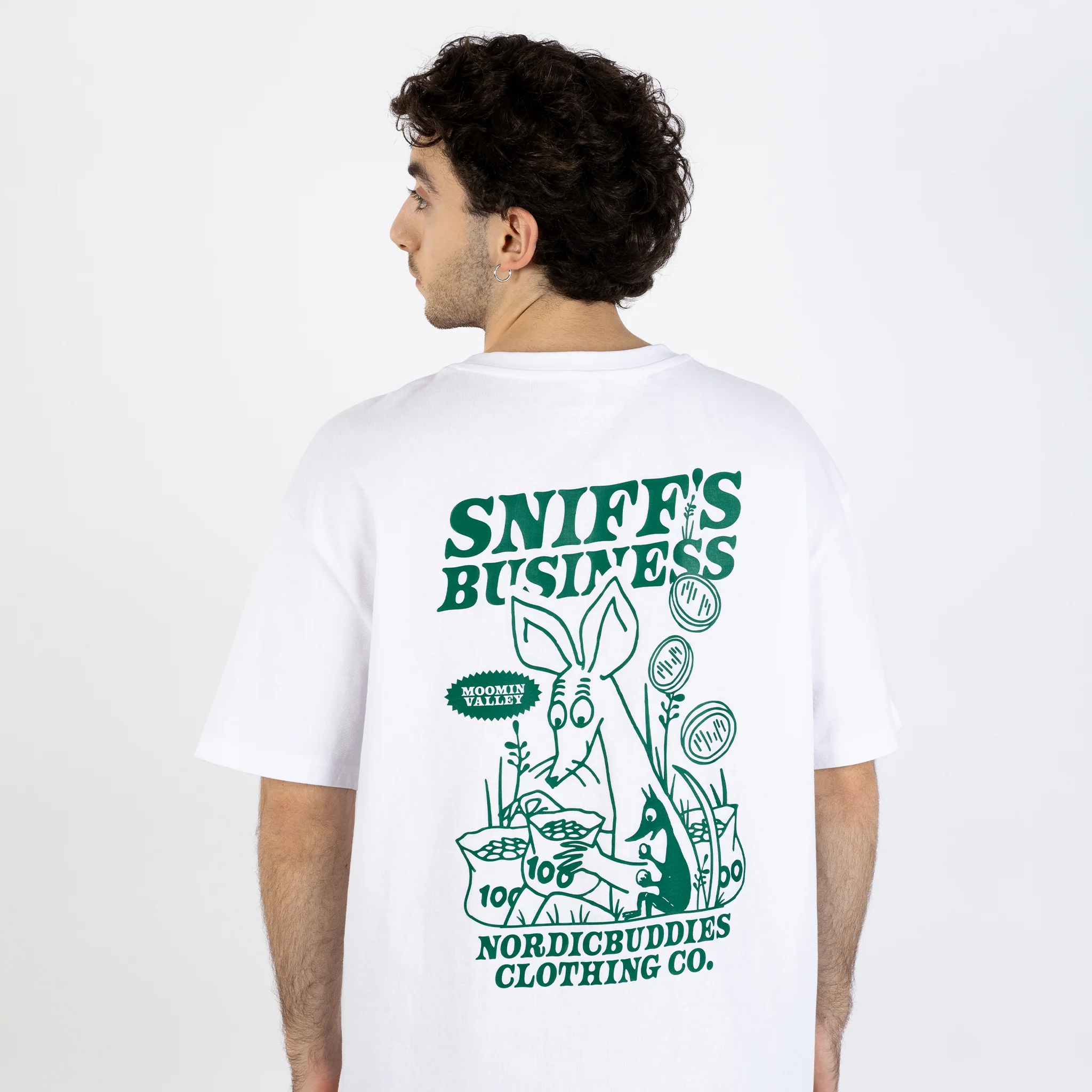 A person faces away, wearing the Moomin Ts - Sniff’s Business: a white tee with a large green cartoon bunny, plants, and SNIFF’S BUSINESS and NORDICBUDDIES CLOTHING CO on the back—ideal for fans of unique styles like Moomin T-shirts. Gate21.ee