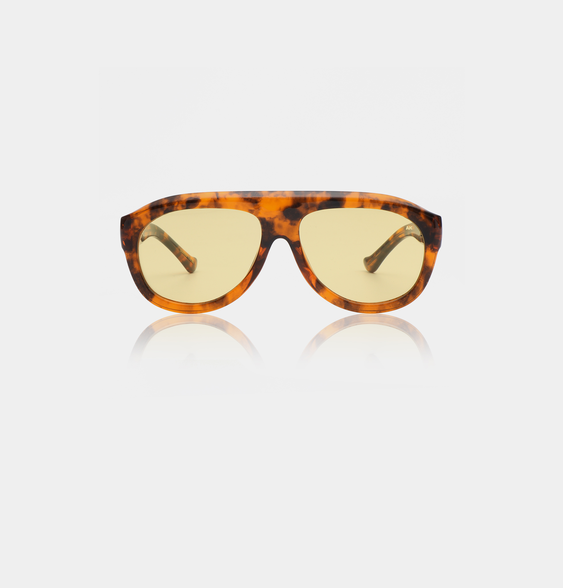 Rio - Havana sunglasses by A. Kjærbede with yellow-tinted lenses are displayed against a white background. The arms curve inwards, and the front frames feature a patterned brown and amber tortoiseshell design. Gate21.ee