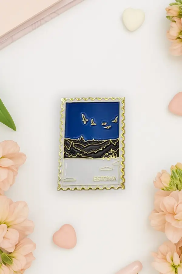 A rectangular magnet designed like a postage stamp features birds flying over a landscape with “Estonia” written at the bottom. Much like the vibrant touches found on a New Rebels small rucksack, this Magnet – talvine mets is surrounded by flowers and heart-shaped objects on a white surface. Gate21.ee