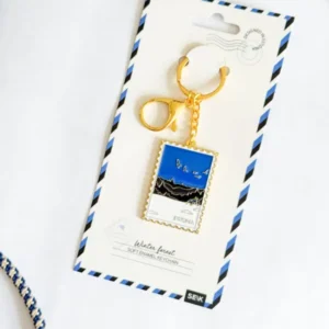 A Võtmehoidja – Talvine mets featuring a gold clasp and a rectangular enamel charm with a blue and black Estonia landscape, presented on a postcard-style card reading “Winter forest” with classic airmail borders—an ideal accessory for your New Rebels small rucksack or as a distinctive travel keepsake. Gate21.ee
