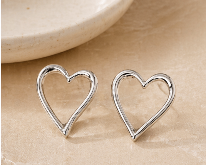A pair of Love - BØLD Earrings - Silver is displayed on a beige stone surface, with part of a round ceramic dish visible in the background. Gate21.ee
