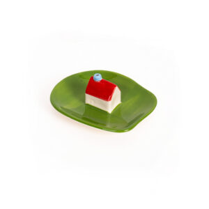 The Incense burner - Milk, a small ceramic house with a red roof and blue chimney inspired by Helio Ferreti’s modern and colourful designs, sits on a glossy leaf-shaped green plate against a white background. Gate21.ee