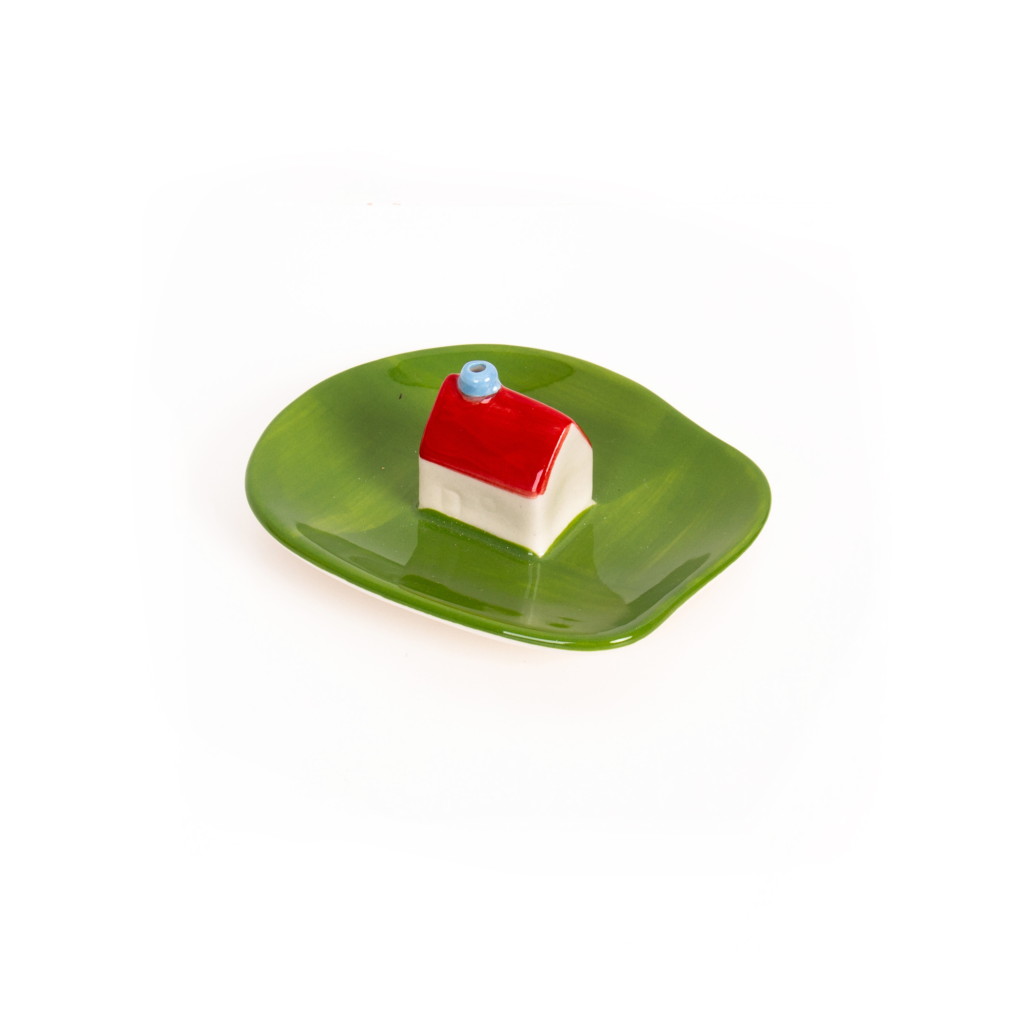The Incense burner - Milk, a small ceramic house with a red roof and blue chimney inspired by Helio Ferreti’s modern and colourful designs, sits on a glossy leaf-shaped green plate against a white background. Gate21.ee