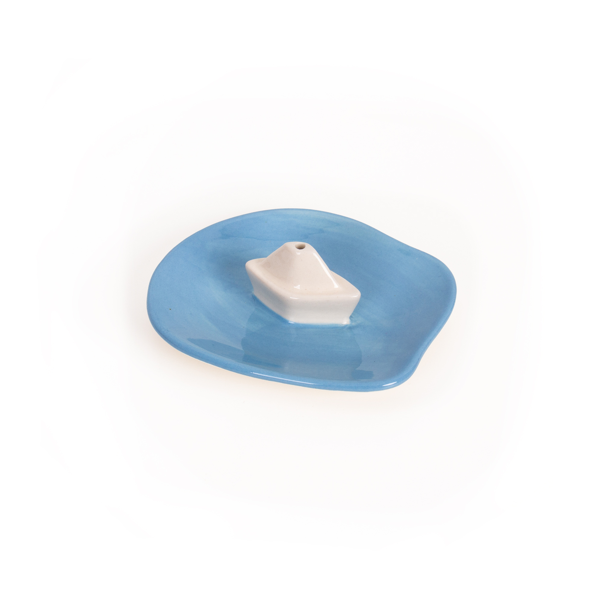 The Incense burner - Boat by Helio Ferreti is a small ceramic dish featuring an irregular blue base and a white cone-shaped holder in the centre, photographed on a white background, showcasing the brand’s modern and colourful incense burners. Gate21.ee
