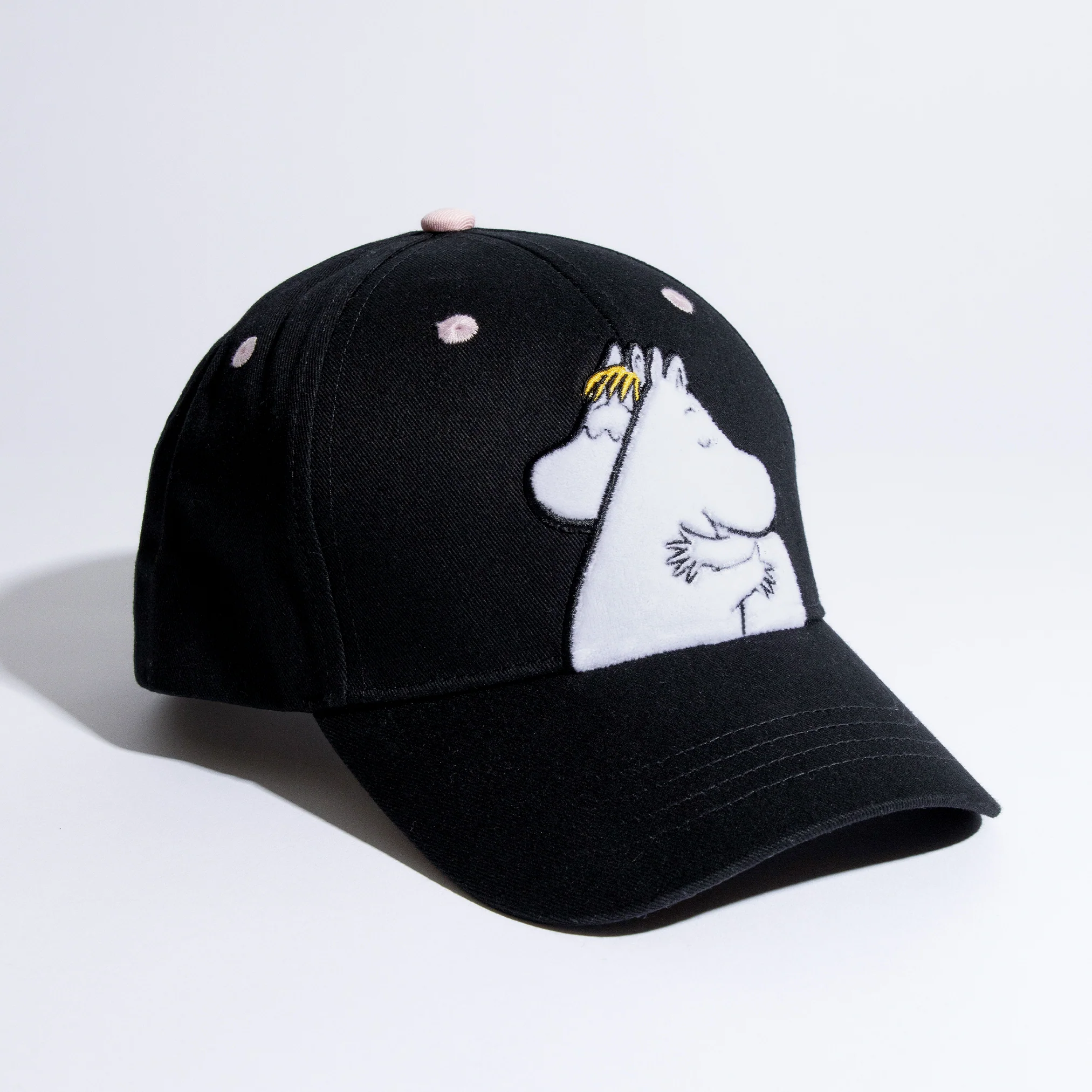 The Moomin Love Kids Cap is a black baseball cap embroidered on the front with a white cartoon character sporting a yellow-striped object on its head. Reminiscent of popular Moomin keyrings, it features pink dots on the crown and is displayed against a plain white background. Gate21.ee
