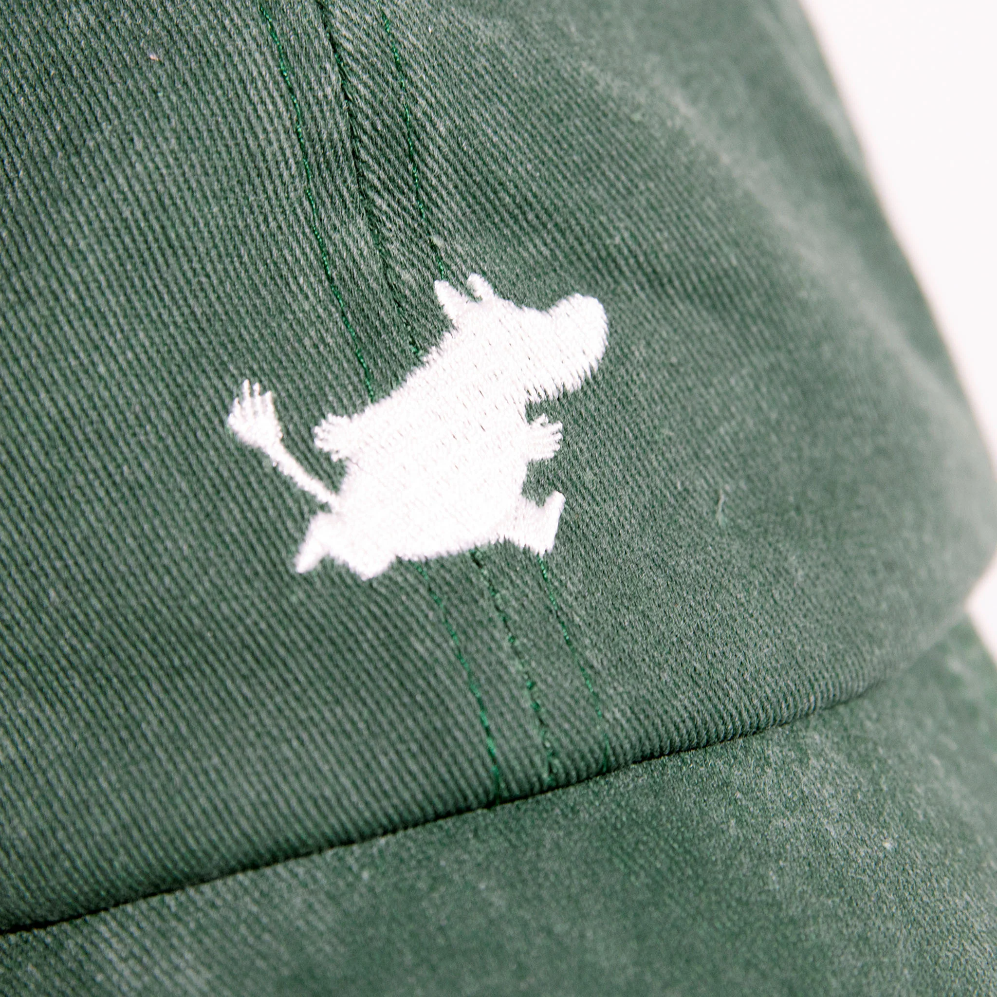 A close-up of the Moomin Cap - Green showcases an embroidered white outline of a cartoon hippo-like character, inspired by the cherished Moomin keyring designs, prominently displayed on the front panel above the brim. Gate21.ee