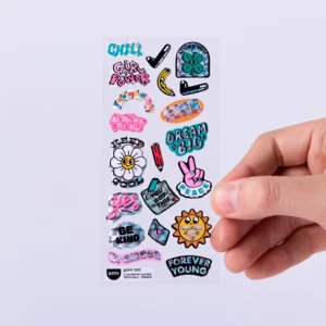 A hand holds a sheet of Letter - Fabulous Stickers by OMY, featuring cheerful, illustrated designs with playful phrases like CHILL, GIRL POWER, and DREAM BIG, alongside vibrant images of flowers, suns, and smiley faces. Gate21.ee