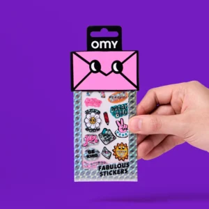 A hand holds a pack of Letter - Fabulous Stickers from OMY, showcasing colourful designs such as flowers, a peace sign, uplifting phrases, and trendy sticker earrings, all set against a solid purple background. Gate21.ee